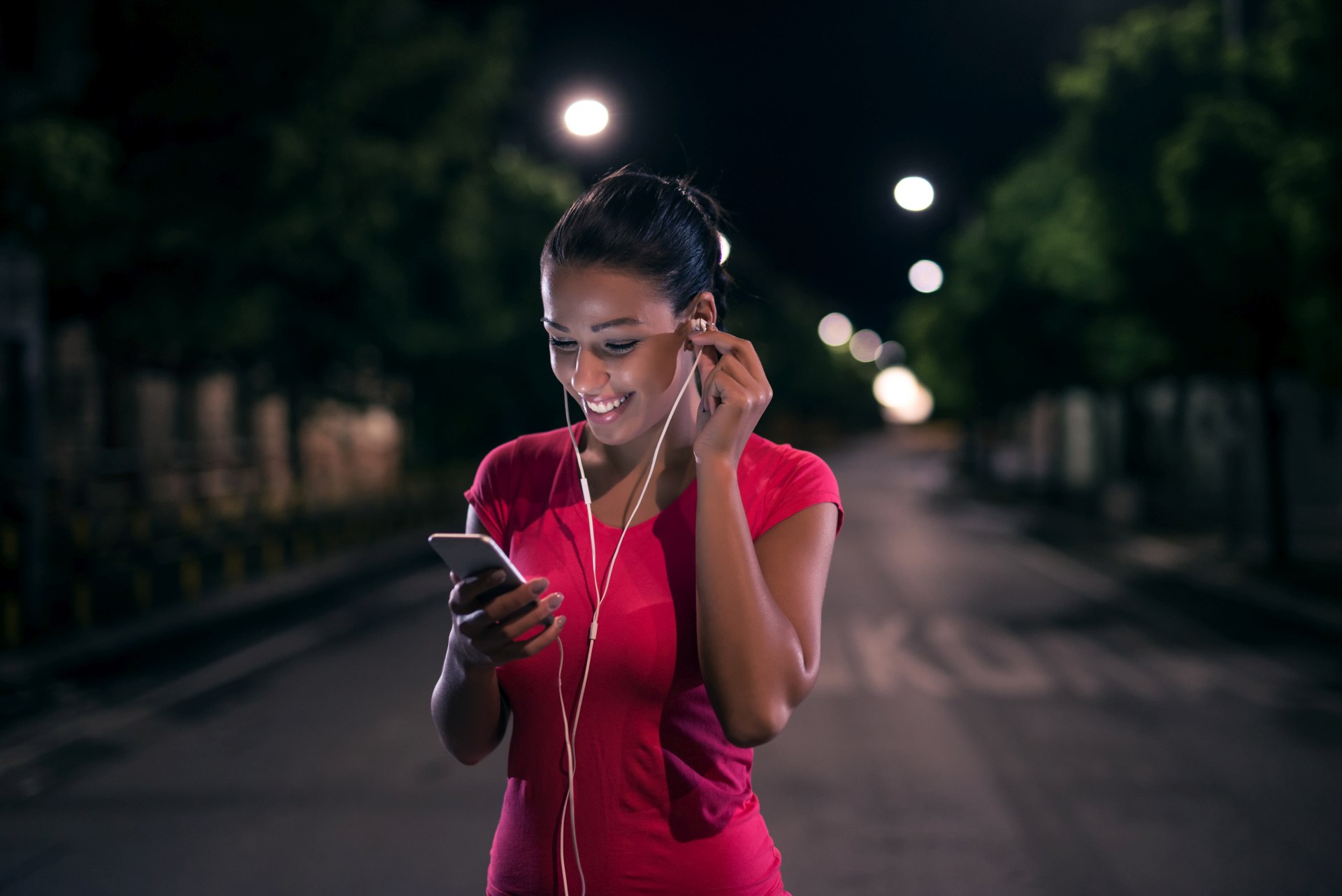 Beautiful young woman jogging at night smiling while looking at her phone